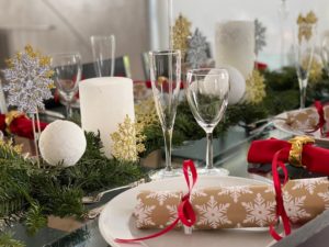 Christmas table is set with Christmas tree greens, gold snowflake Christmas crackers, and pillar candles and styrofoam balls covered with epsom salt to resemble snow.