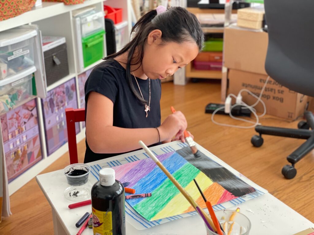 Child paints black poster paint over crayon to make crayon scratch art.