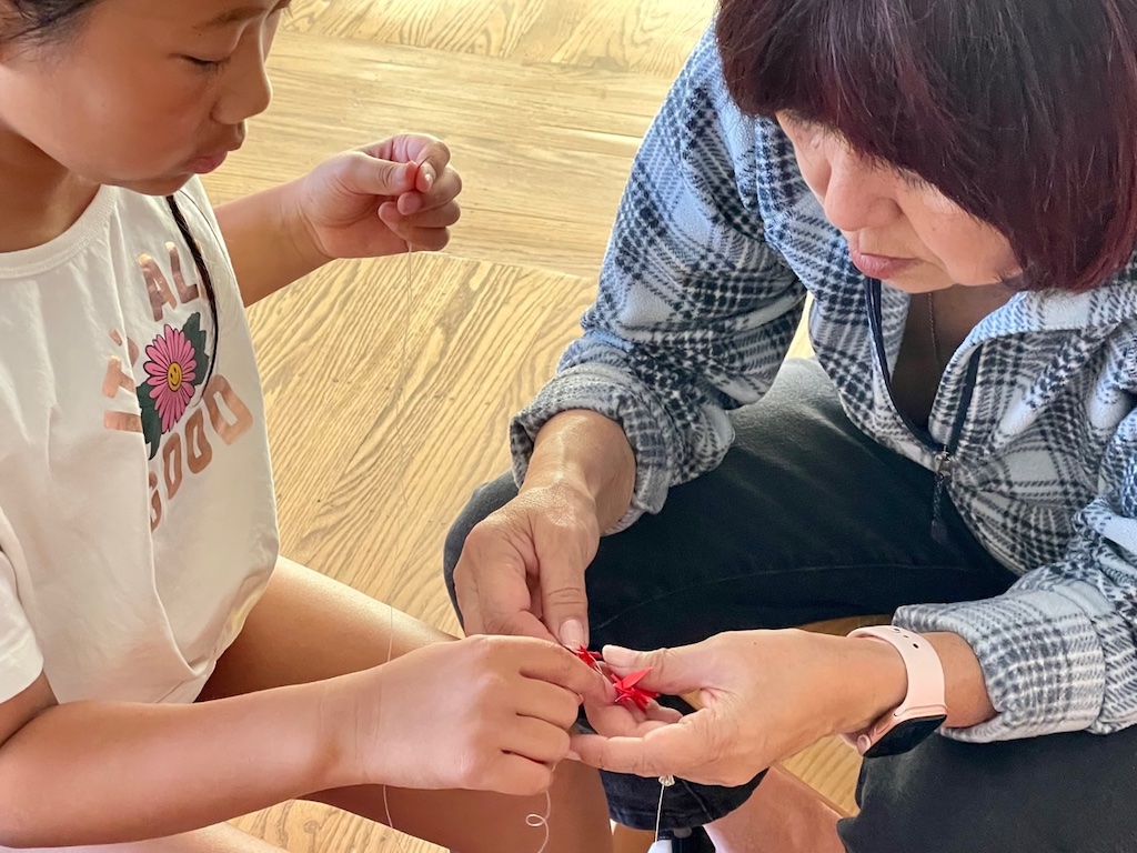 Grandma helps child to string mini origami cranes.