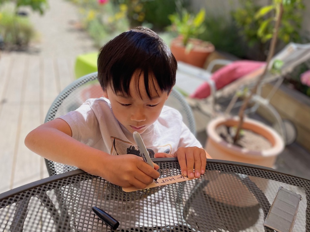 Child writing the name of the bug hotel on a wooden tongue depressor with a Sharpie.