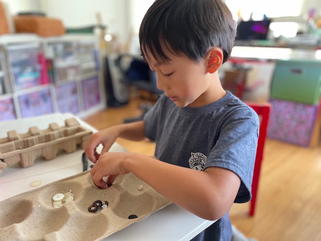 Child organizes button game pieces to play on apple tray board.