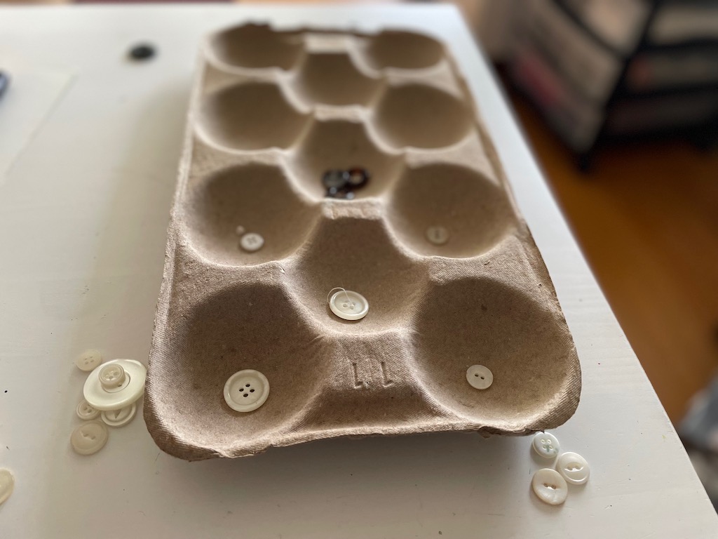 Tray from an apple box is used as a game board, along with black and white buttons.