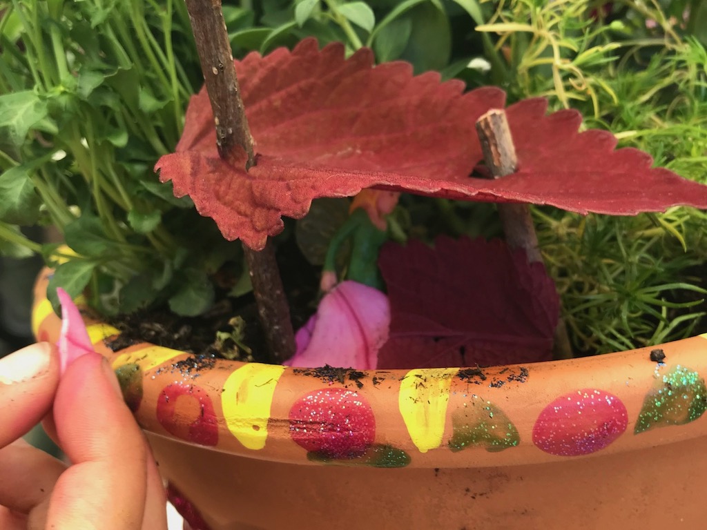 Fairy garden has a house made of a large leaf, held up by twigs.