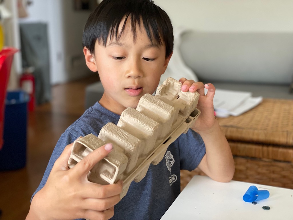 Child looks for ways to join toner cartridge inserts together to create a troop carrier.