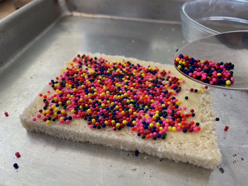 Spoon sprinkles over buttered bread set in a cookie sheet to contain errant sprinkles.