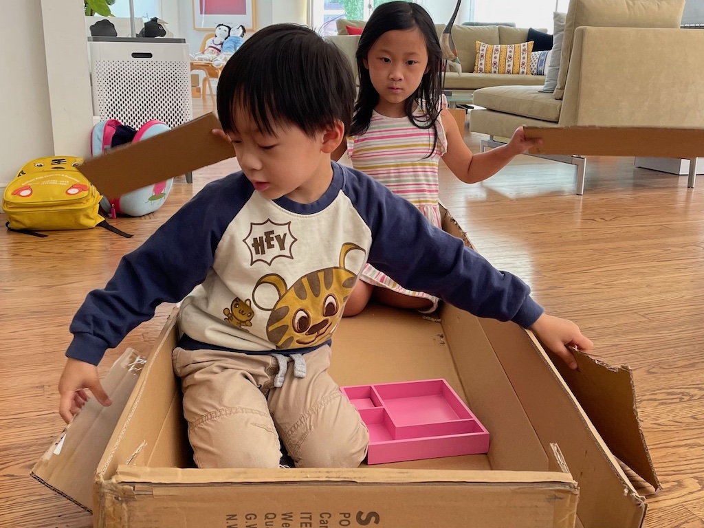 Kids sitting in a shallow box pretending to be rowing out to sea. Box flaps were cut from the box to use as paddles.