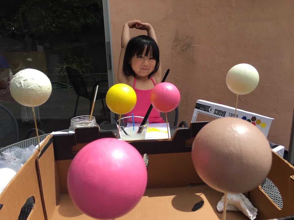 Child paints styrofoam balls and dries them in the corrugated ridges of a box.