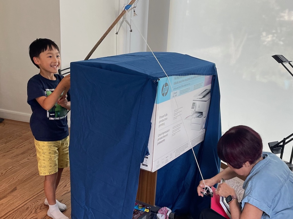 A big box covered in a blue sheet becomes the sea; kids with yardstick poles go fishing. Grandma gives them trash or treasure.