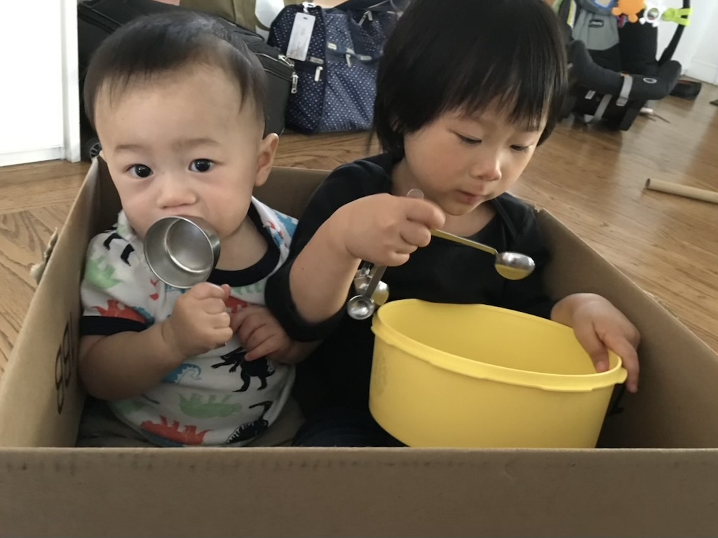 Children sitting in a box play with kitchen tools.