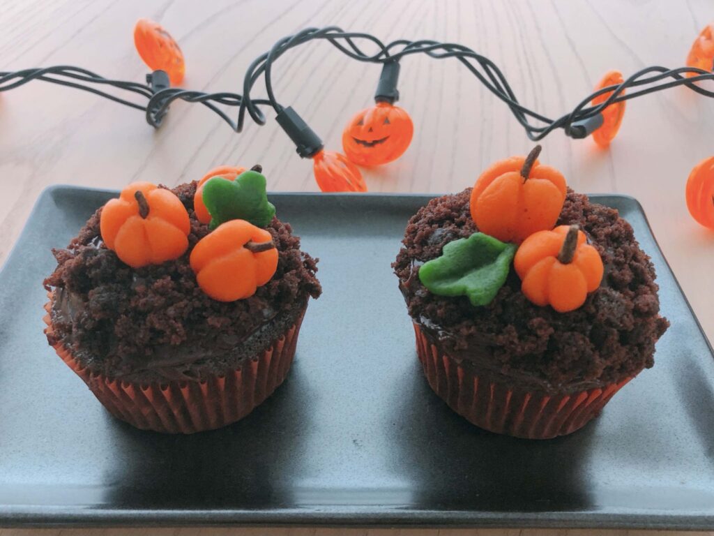 Cupcakes are sprinkled with crushed chocolate cookies for dirt, with pumpkins made from marzipan dough planted on top.