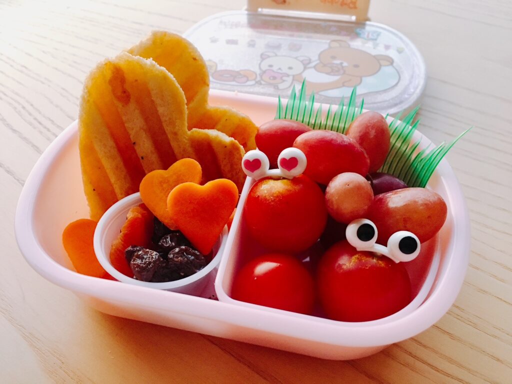 Bento of cherry tomatoes with eyes, carrot hearts, and heart-shaped sandwich.