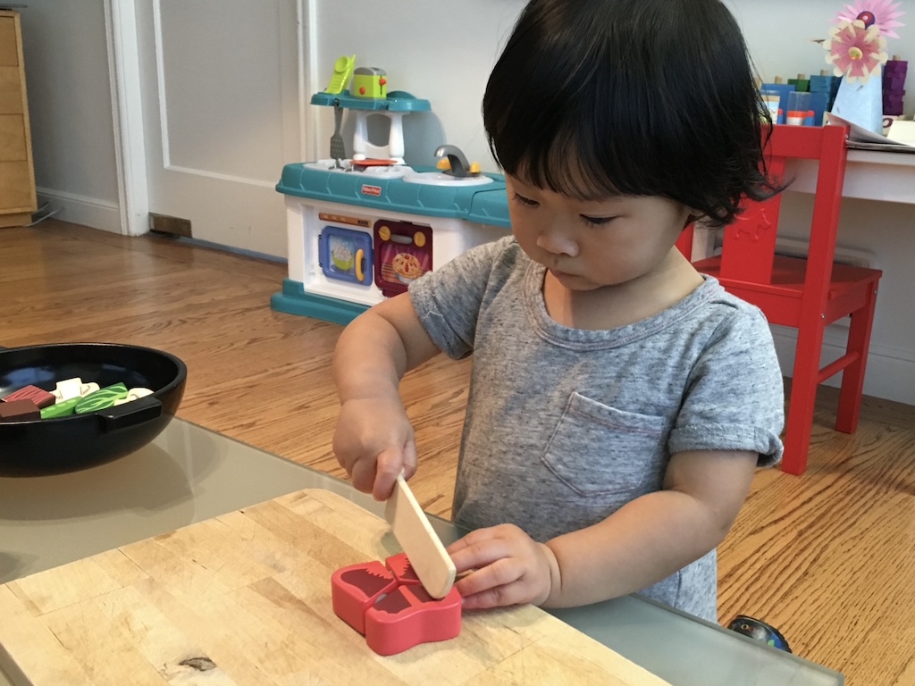 To cook with a grandchild over the holidays, start them early with cooking play. Toddler cuts a wooden bell pepper to make a stir-fry.