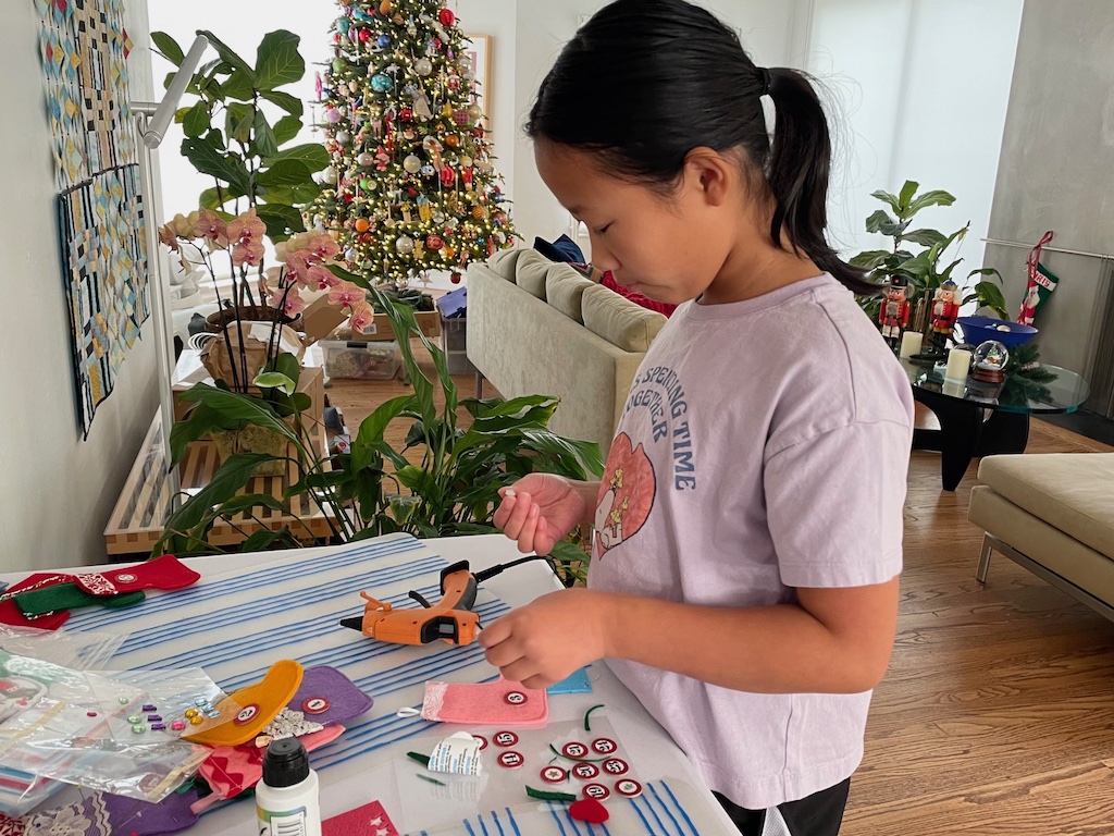 Child adheres trim with a glue gun to decorate small Christmas stockings for an Advent calendar.