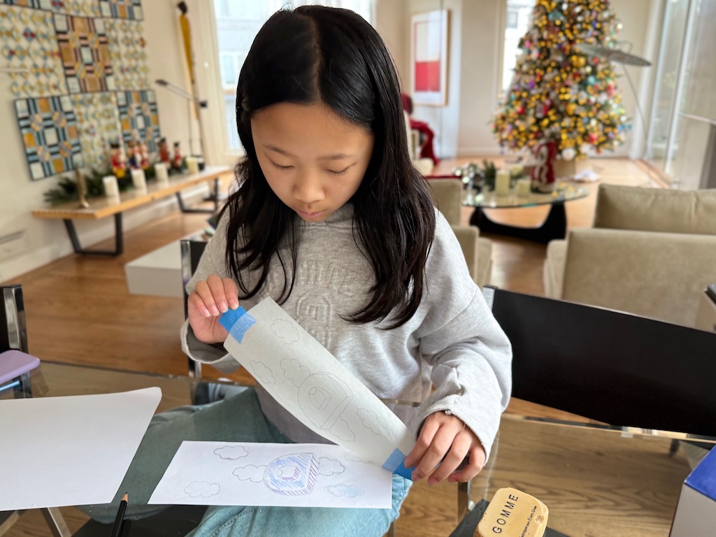 Child tapes tracing paper over her design.