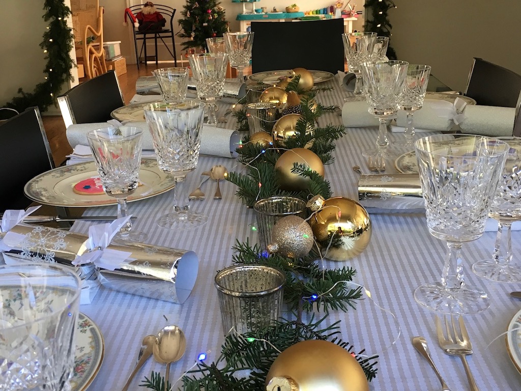 A simple table setting features gold balls of different sizes on a bed of Christmas tree greens, with tea lights interspersed.