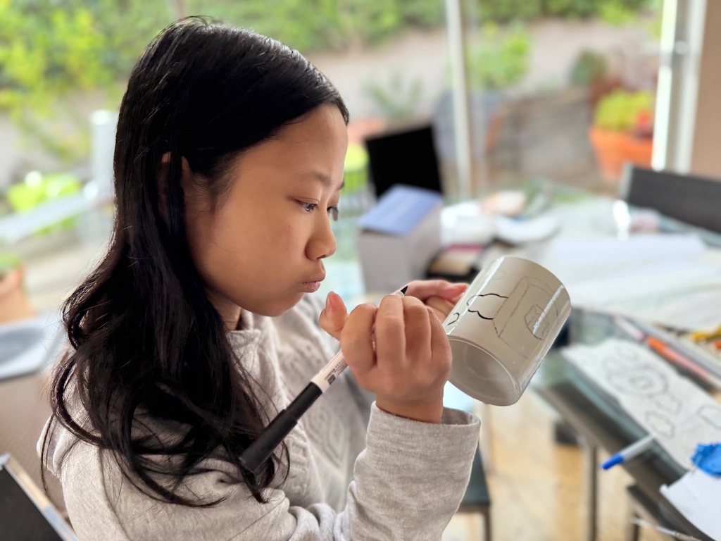 Child goes over the lines with the ceramic pen to complete the mug project.