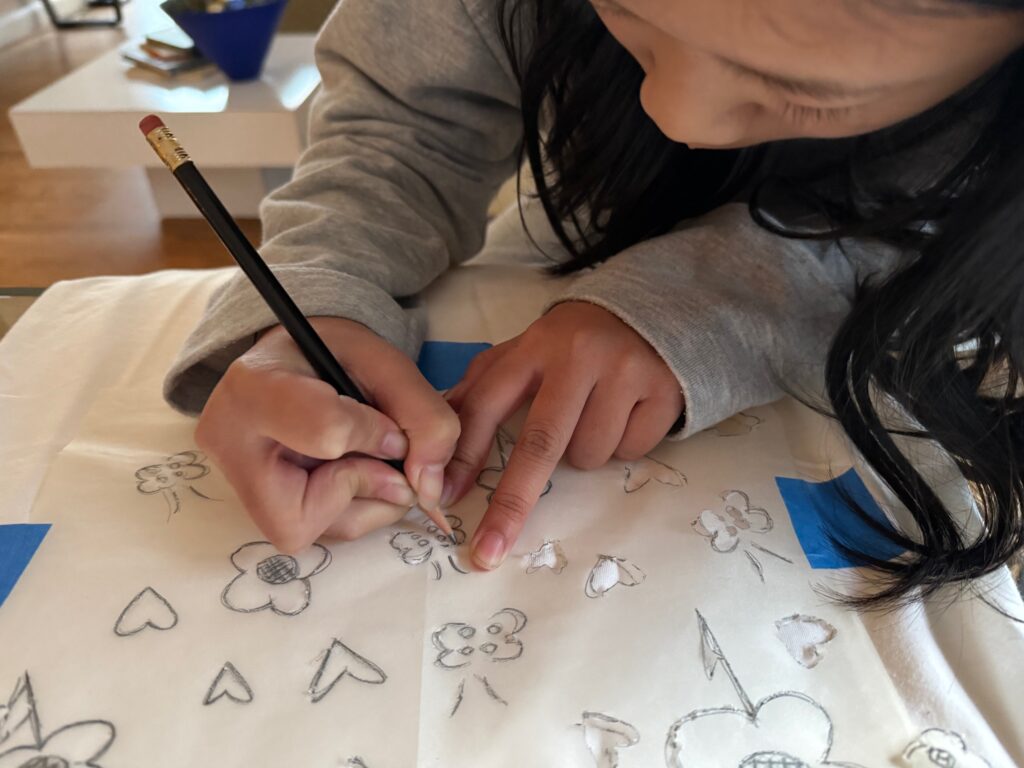 Child traces lines of her design onto white T-shirt. She'll color the lines next.