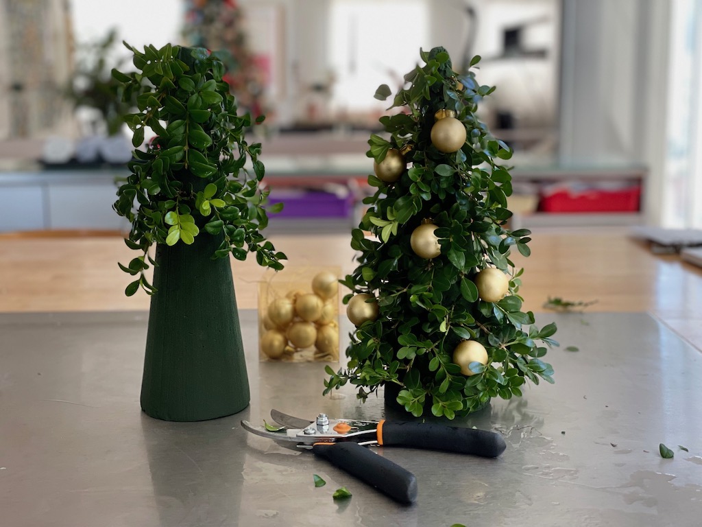 Greens are being poked into wet styrofoam cones for Christmas tree centerpieces.