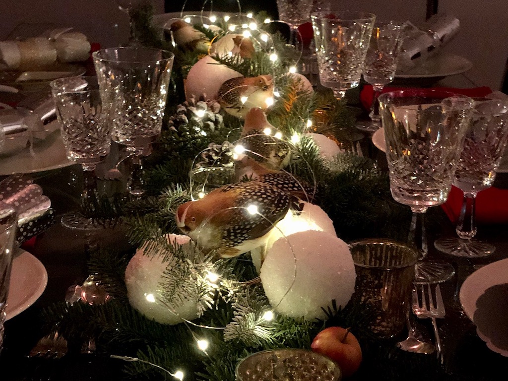 Greens scrounged from a Christmas tree lot make a table runner. Epsom-salt-coated styrofoam balls mimic snowballs.  Partridges, and pinecones add to the woodland effect. Fairy lights add sparkle.