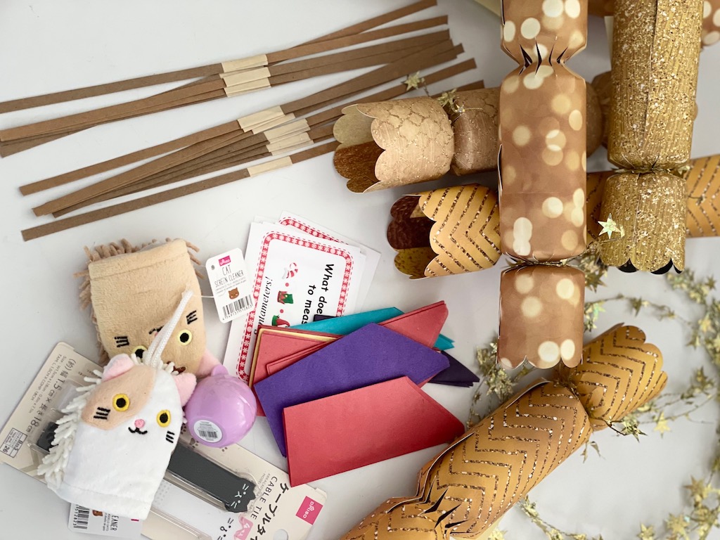 Elements for making Christmas crackers: cracker snap strips, tissue paper crowns, joke slips, and little gifts.