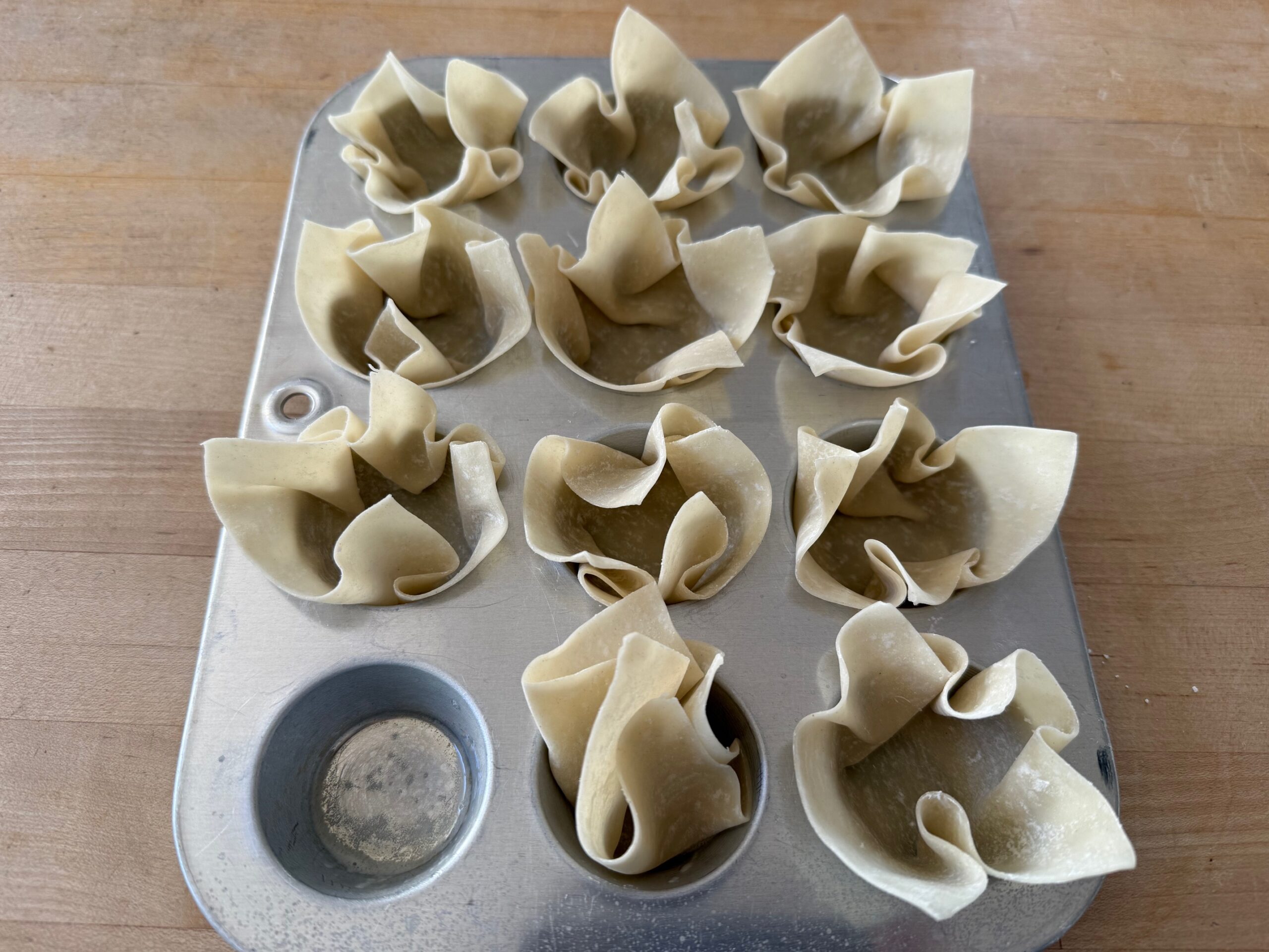 To make wonton cups, hold four corners of a wonton wrapper and drop it into a mini muffin tin, as the bottom middle muffin cup illustrates.