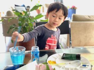 Child paints a discarded spice jar with acrylic paint to make a bud vase.