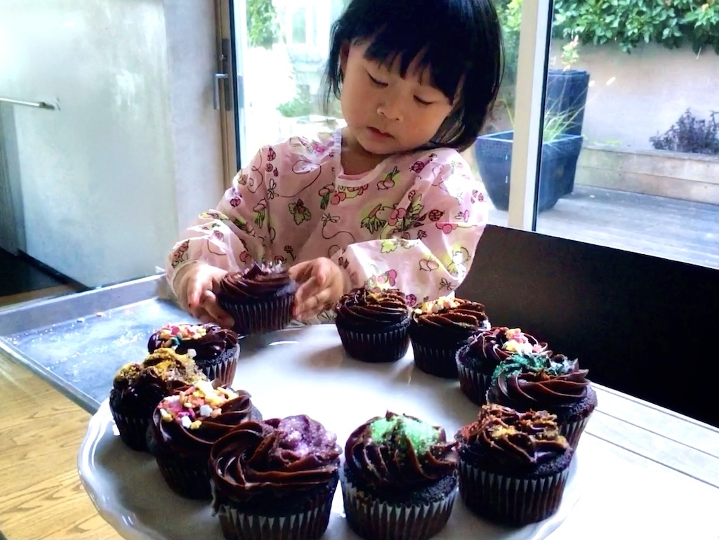 Three-year-old decorates birthday cupcakes for a family birthday party.