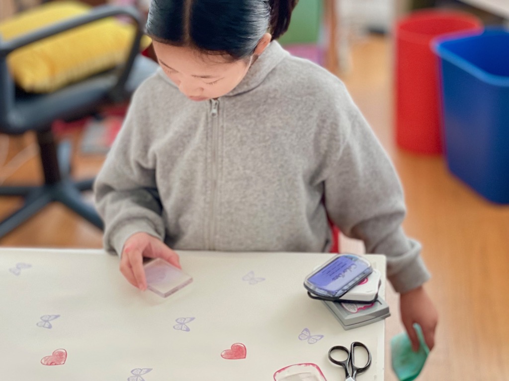 Child stamps a roll of easel paper with butterfly and heart stamps to make Valentine's gift paper.