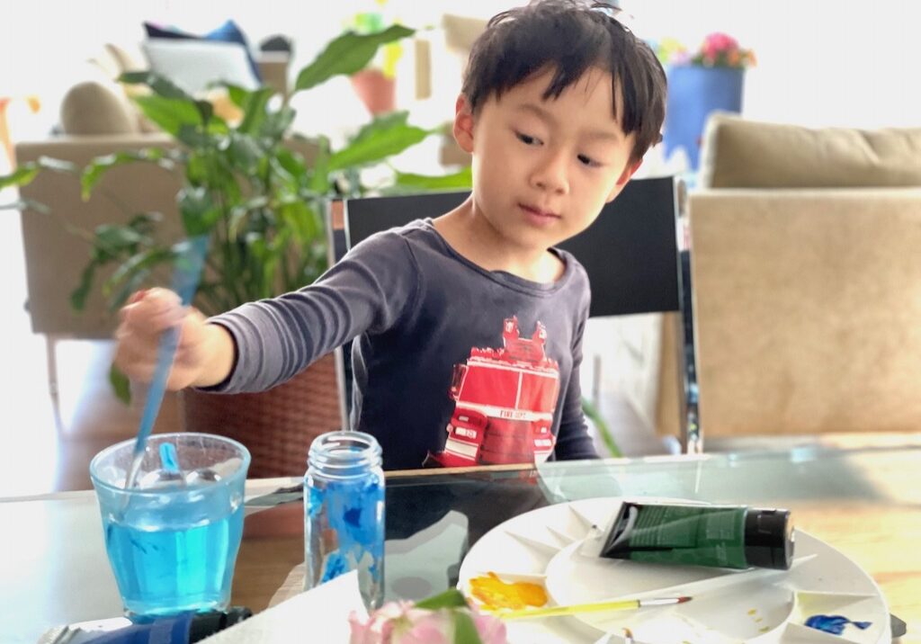 Child paints a discarded spice jar with acrylic paint to make a bud vase.