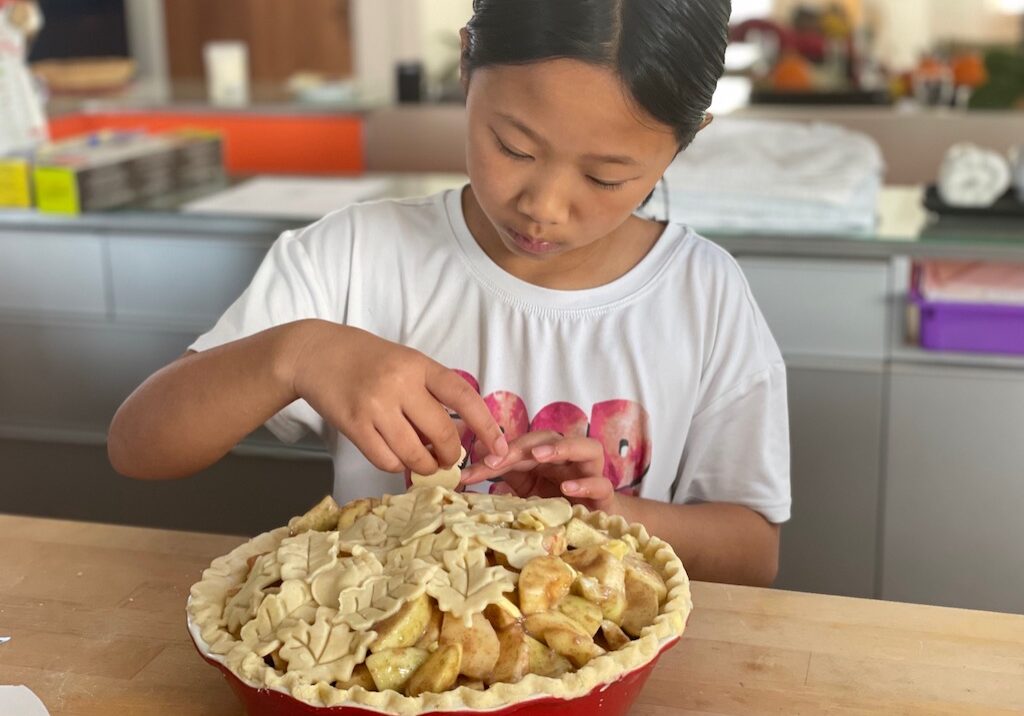 Child adds pastry leaves to an apple pie for Thanksgiving.